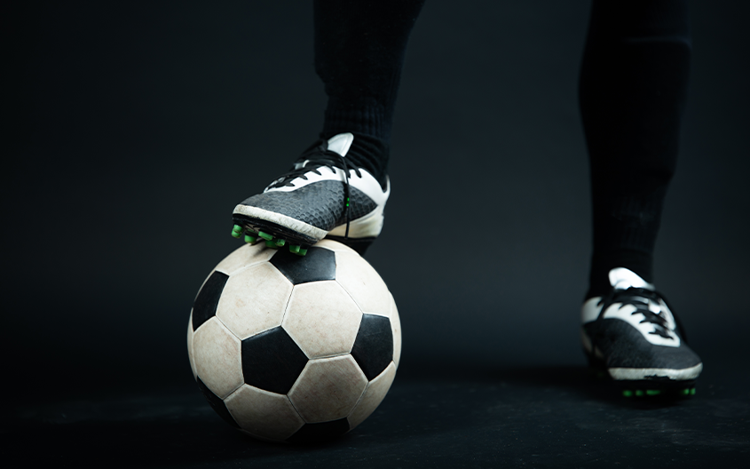 A close-up shot of a football player resting their cleat on a football, reflecting the intense technical foundation taught during Silver Studs FC's 12-hour weekly training blocks.