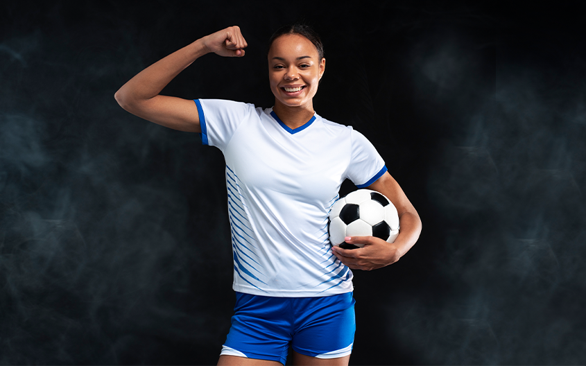 A smiling female football player flexing her right bicep, illustrating the strength and resilience emphasized in Silver Studs FC's youth defensive guide.